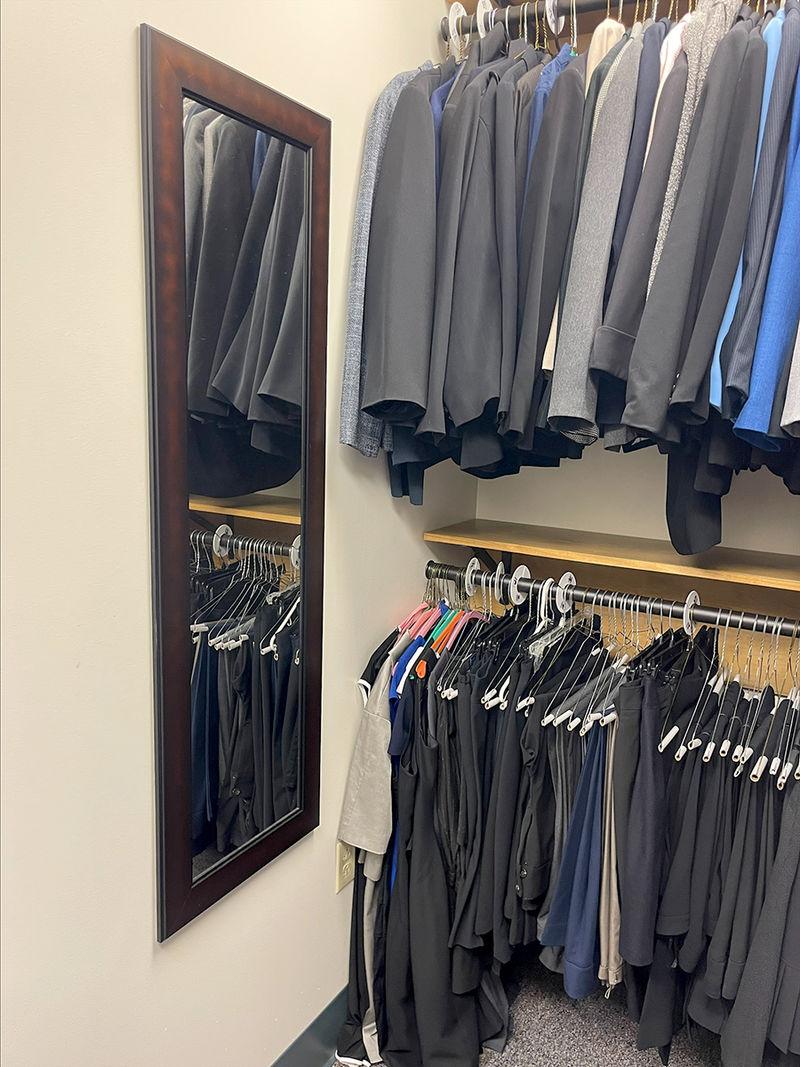 A full-length mirror hanging on a wall near a double-decker rack of men's suit jackets